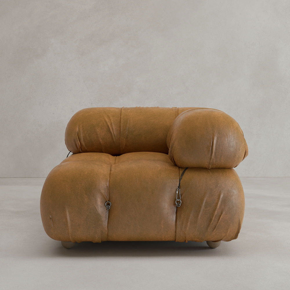 The Belmont Sofa Left Armrest features plush tan leather, rounded cushiony shapes, and visible connecting straps, evoking iconic classic style against a light beige background.