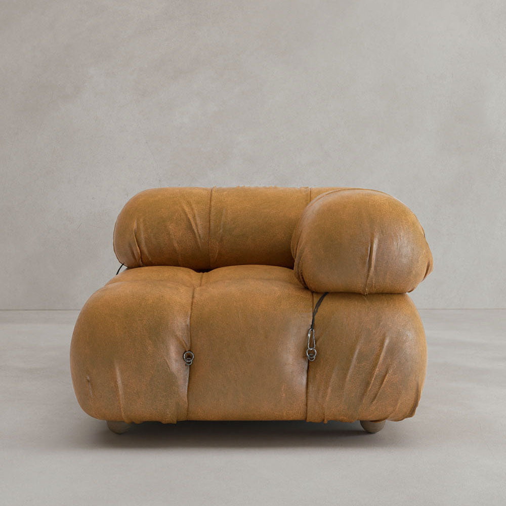 The Belmont Sofa Left Armrest features tan upholstery, overstuffed marshmallow curves, and iconic black straps, creating a classic look against a plain beige background.