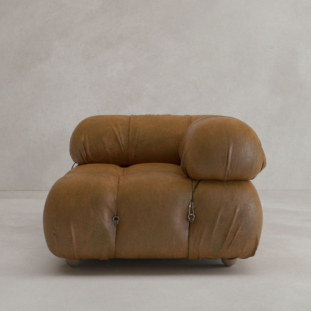 The Belmont Sofa Left Armrest features plush, oversized brown leather with marshmallow-like curves and visible tufted details, set against a plain light beige background.