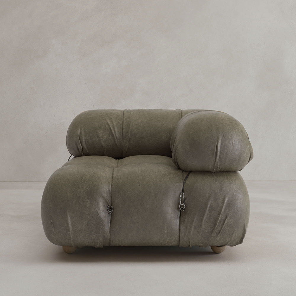 The Belmont Sofa Left Armrest features plush, olive-green upholstery and marshmallow-like curves. Its iconic oversized design includes rounded, tufted details, visible seams, small metal accents, and sits against a light wall.