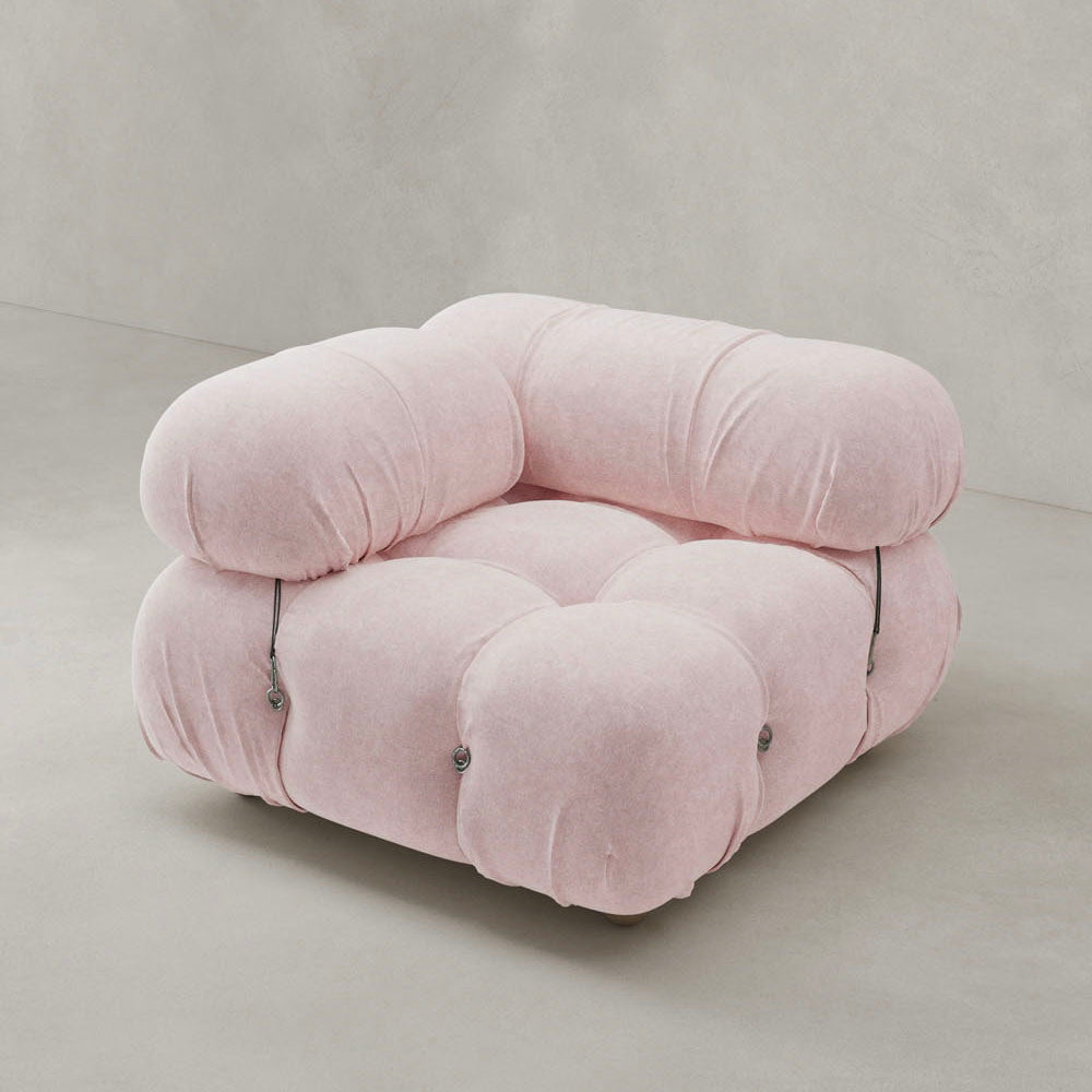 The Belmont Sofa Right Armrest features soft, tufted pink upholstery and a rounded, cushion-like design, adding iconic classic style to your space on a light grey floor against a matching grey wall.