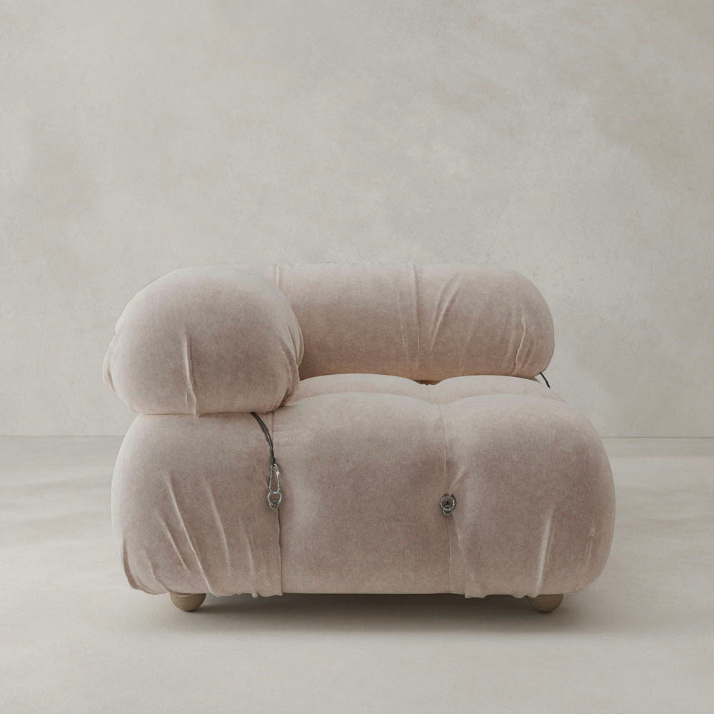 The Belmont Sofa Right Armrest features plush, light beige upholstery with rounded, overstuffed cushions and visible metal fasteners in a modular design, set against a simple, light-toned wall and floor.