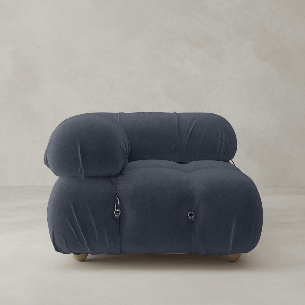 The Belmont Sofa Right Armrest features a modern, low-profile silhouette with plush, rounded lines and modular design. Upholstered in dark blue fabric, it includes visible metal fasteners and wooden feet for a stylish touch against light backgrounds.