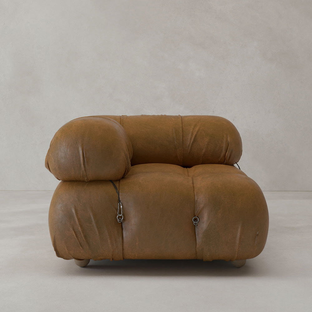 The Belmont Sofa Right Armrest is a spacious, modern piece with soft, rounded light brown leather cushions, modular features like visible stitching and metal fasteners, positioned against a simple, light-colored wall and floor.