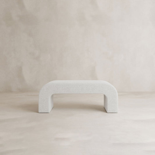 The Beverly Bench, a minimalist white boucle seat with an arched base, is set against a light beige textured background, lending modern elegance to this simple, contemporary space.
