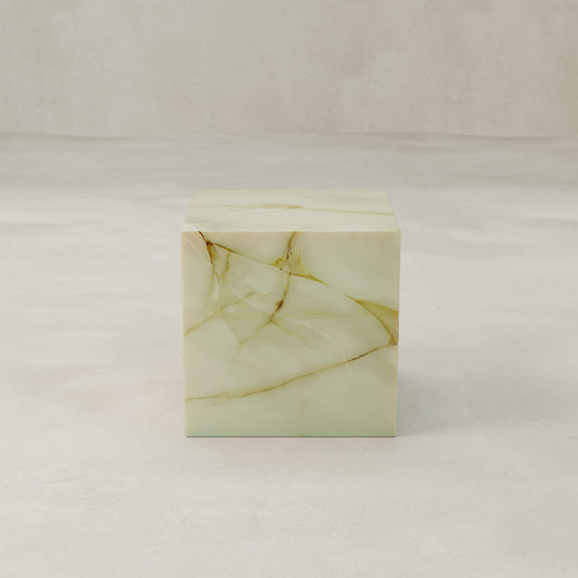 The Blanchaire Onyx Plinth - Cube features light green marble onyx with brown and gold veining, set on a smooth, pale surface against a neutral background—a striking sculptural accent for any space.