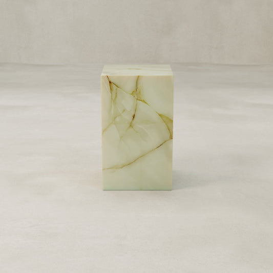 The Blanchaire Onyx Plinth - Tall features a luminous finish and delicate veining in pale green and gold, set on a smooth light surface against a neutral backdrop.
