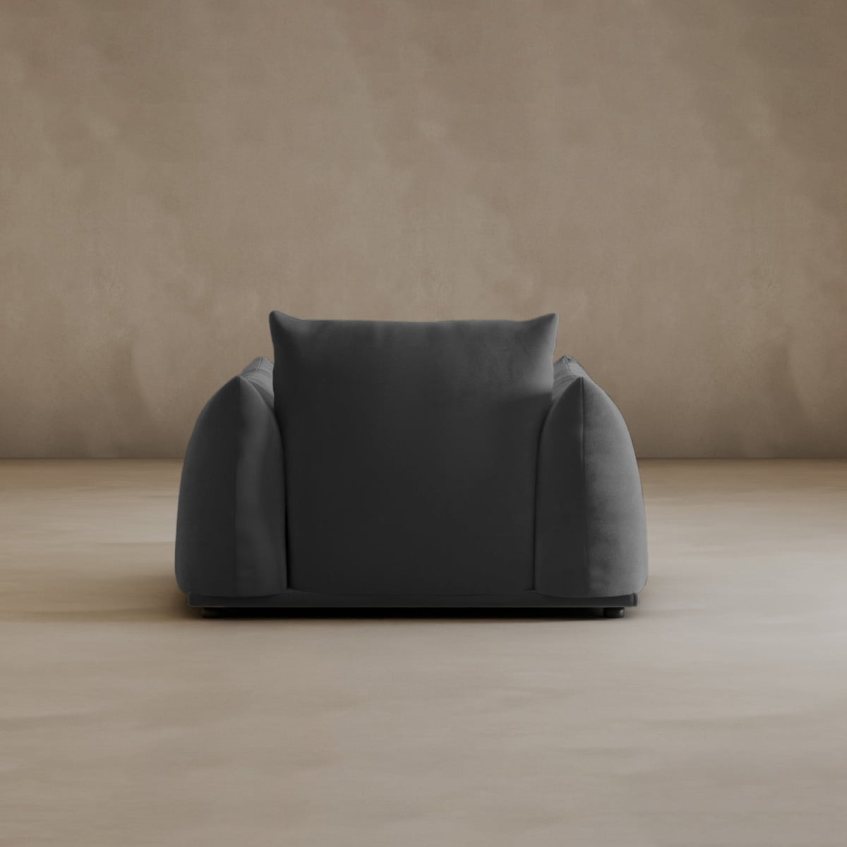 The Calypso Arm Chair features plush dark gray upholstery, wide rounded arms, and a square backrest, adding modern elegance to minimalist rooms with beige walls and floors.