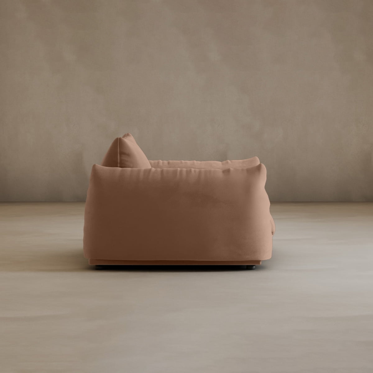 The Calypso Arm Chair, shown in plush light brown with a single cushion and viewed from the side against a beige wall and floor, embodies modern elegance in a minimalist setting.