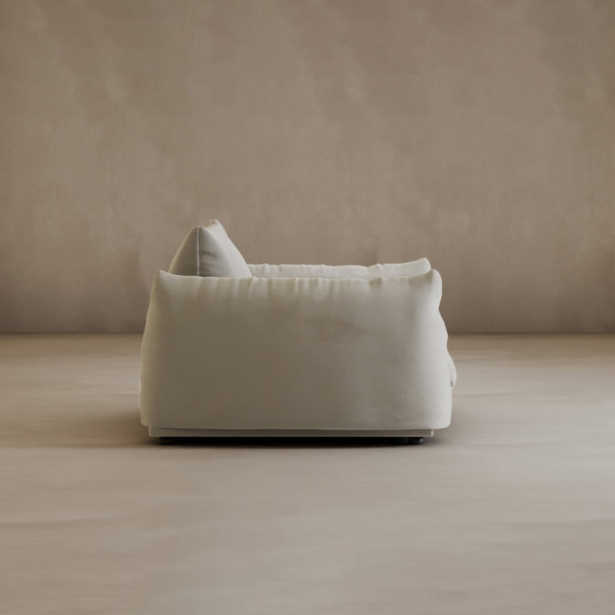 The Calypso Arm Chair, featuring modern elegance and plush comfort, is viewed from the side against a matching beige wall and floor in a minimalist, empty room.