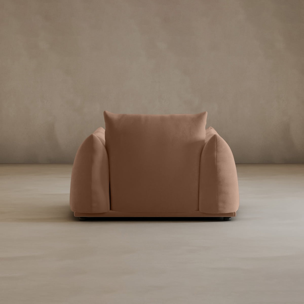 The Calypso Arm Chair showcases modern elegance with its oversized shape, plush comfort, and rounded edges in brown fabric, perfectly set against a plain light beige wall and floor.