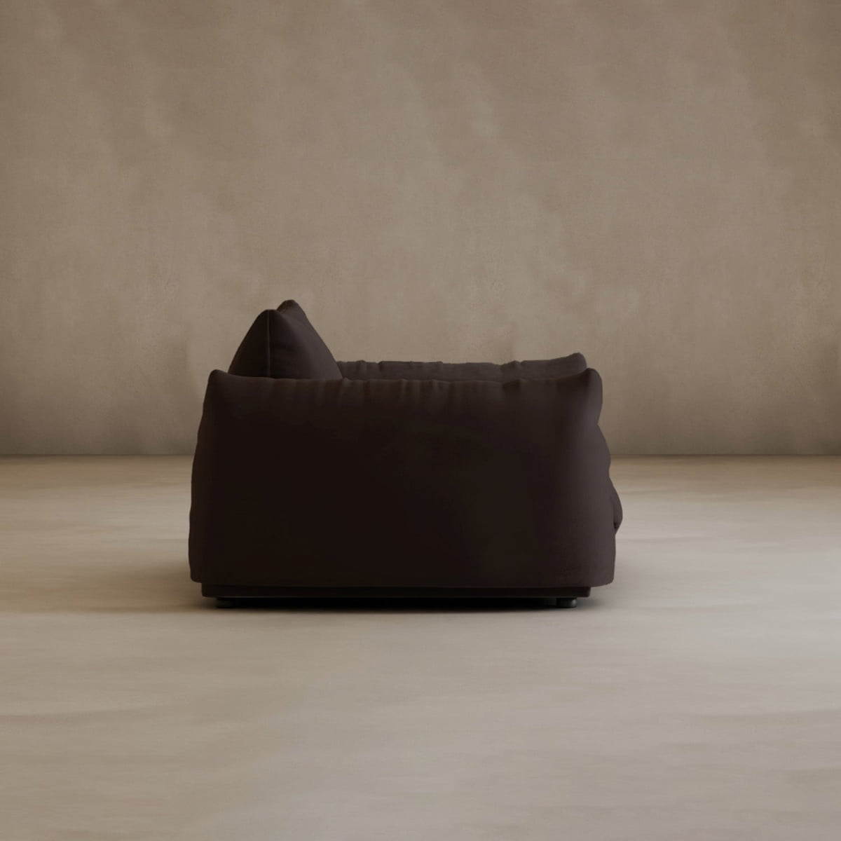 The Calypso Arm Chair, in dark brown with plush cushions, is shown in profile against a plain beige wall and floor in a minimalist room, radiating modern elegance.