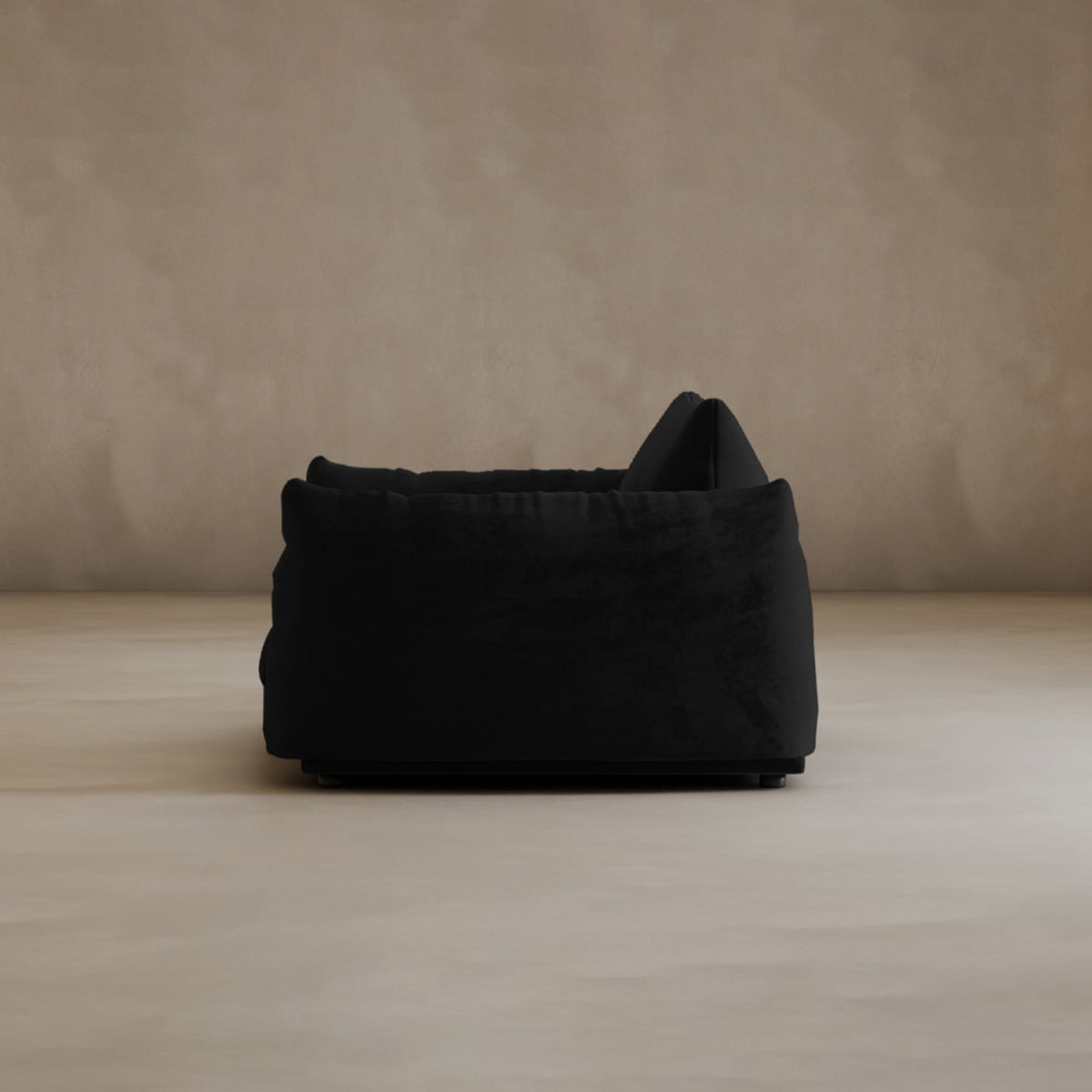 The Calypso Arm Chair, seen from the side, features plush cushions and a modern black design, set against a beige wall and light floor—an elegant embodiment of contemporary style and comfort.