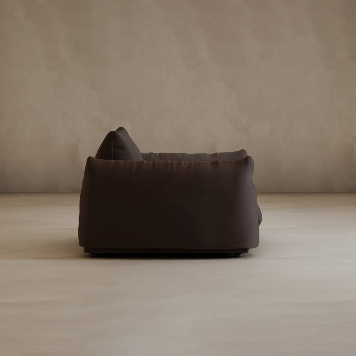 The Calypso Arm Chair, in modern dark brown with plush cushioning, exudes comfort and elegance—seen from the side against a beige wall and light floor in a minimalist setting.