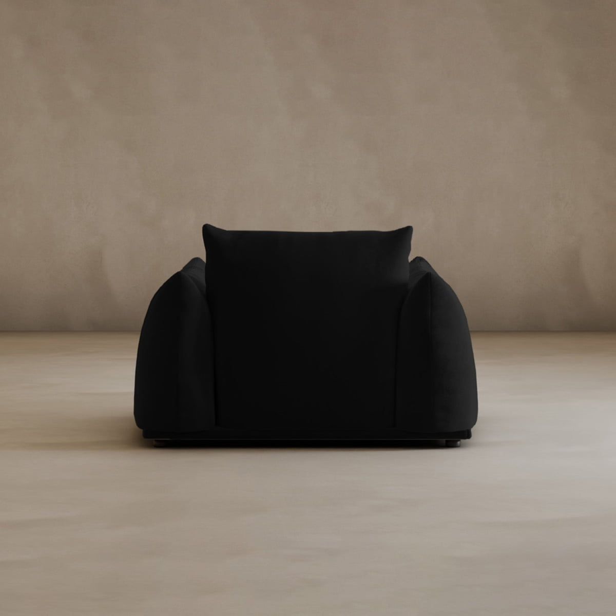 The Calypso Arm Chair, a modern oversized black armchair with plush cushions, stands centered in a minimalist space with light beige textured walls and floor, exuding contemporary elegance.
