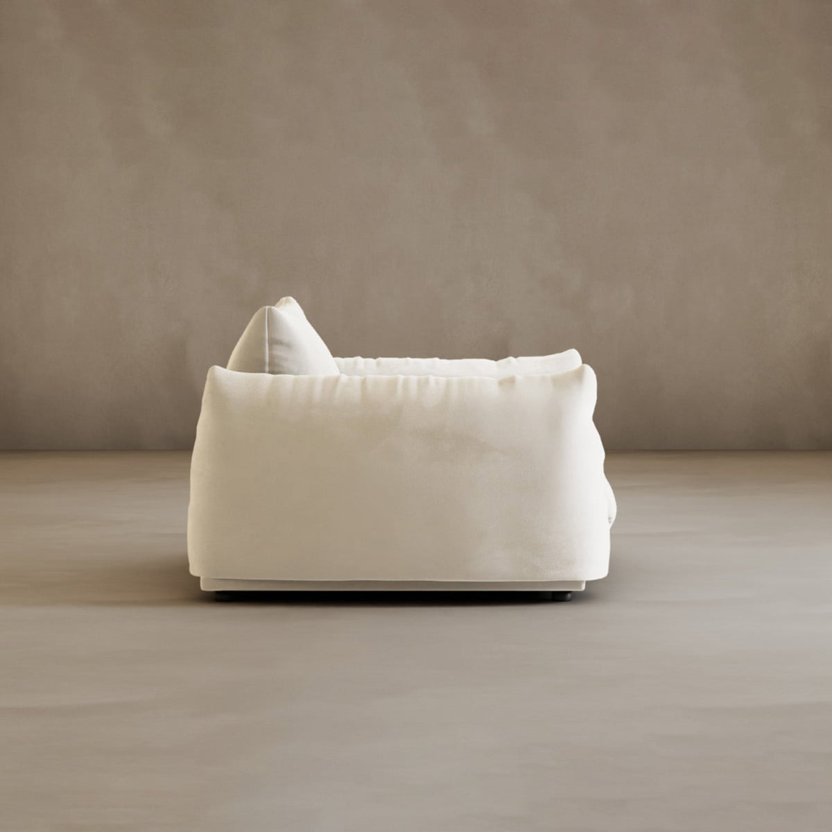 The Calypso Arm Chair, plush and white with soft, rounded lines, exudes modern elegance as its shown from the side against a plain light beige wall and matching floor.