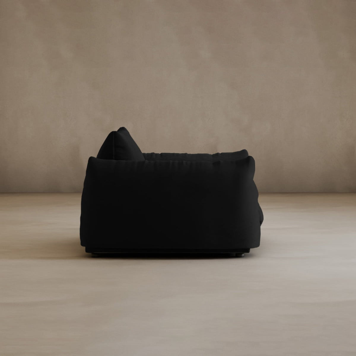 The Calypso Arm Chair, shown from the side, features a modern black design with plush comfort and soft cushions, set on a light beige floor against a neutral textured wall.