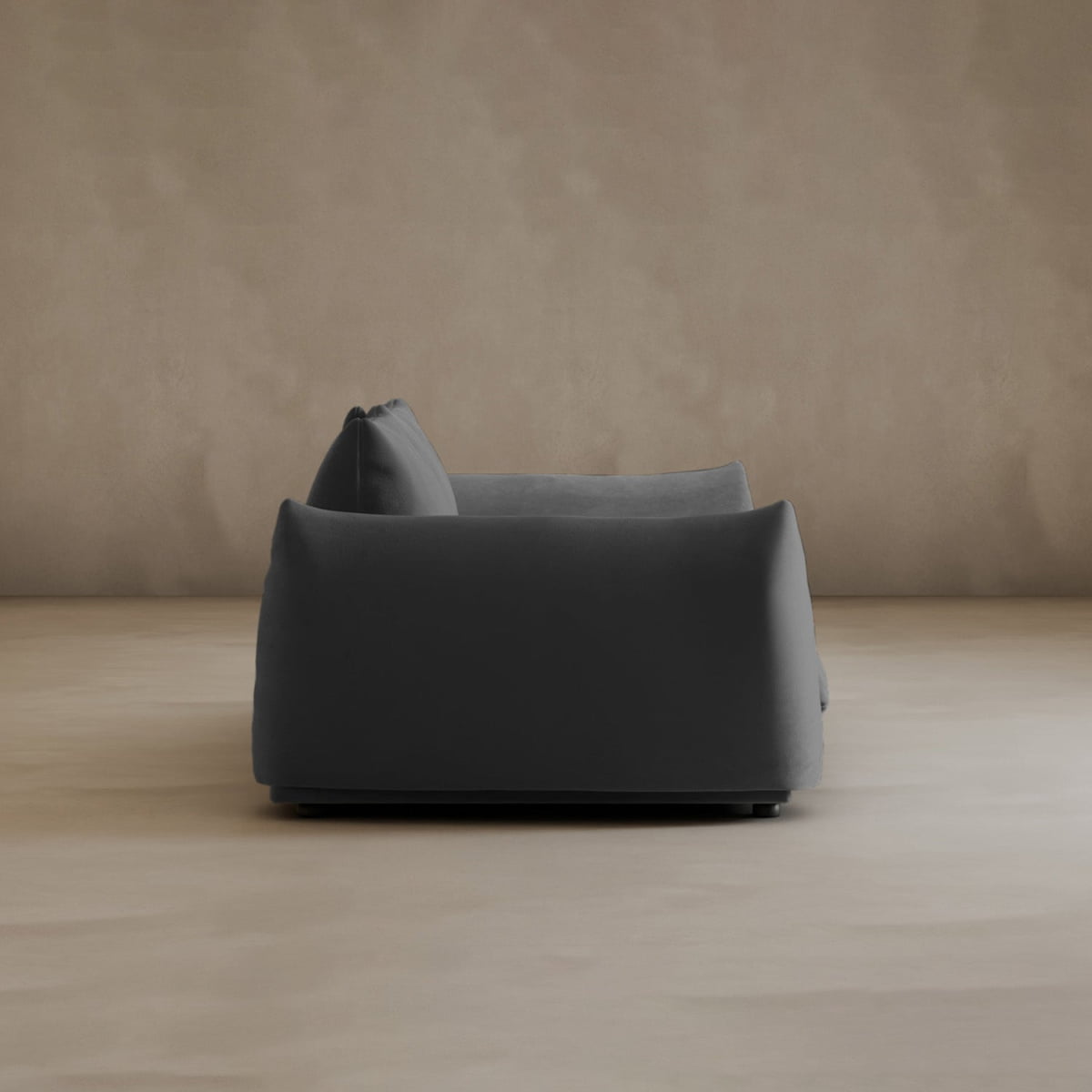 A modern, dark gray Calypso Loveseat exudes elegance, seen from the side against a plain light beige wall and floor in a minimalist setting.