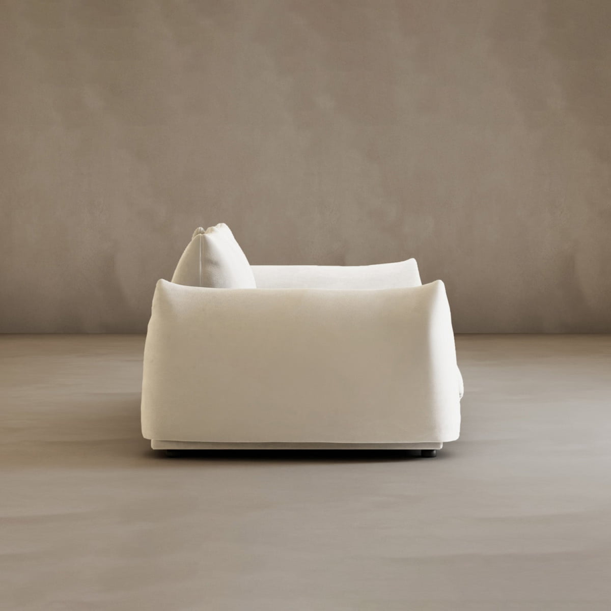 The Calypso Loveseat, featuring modern white upholstery and soft, rounded edges, is shown from the side against a plain taupe wall and floor, showcasing contemporary elegance.
