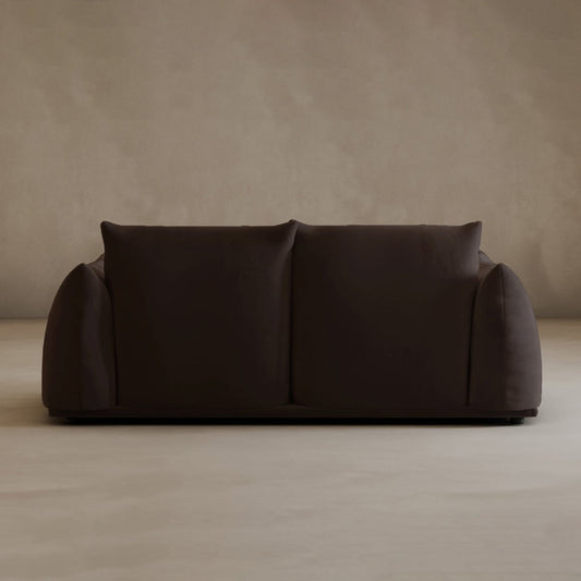 Modern elegance shines through the dark brown Calypso Loveseat, featuring plush, rounded cushions and wide armrests, set against a plain light beige wall and floor.