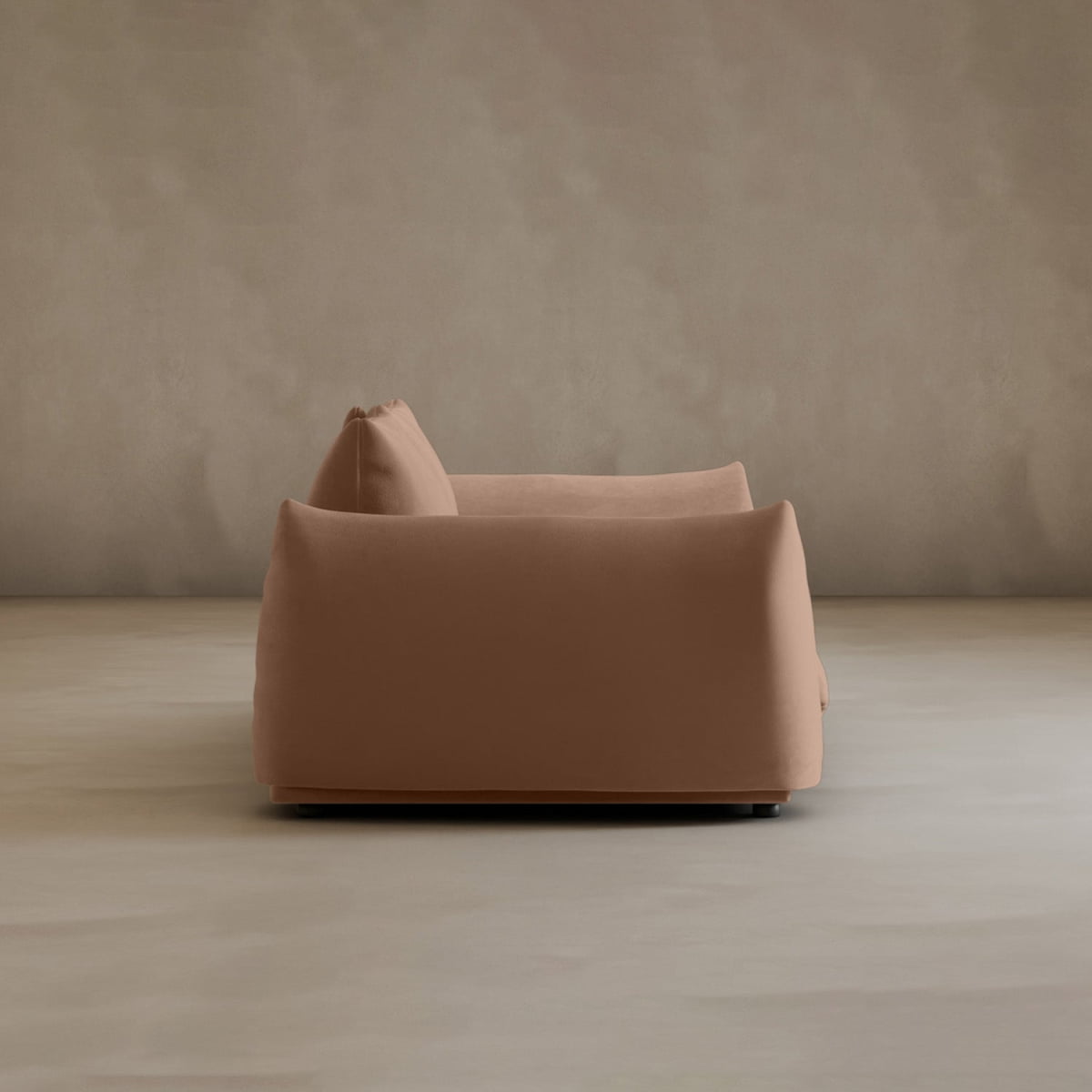 A modern, minimalist Calypso Loveseat with soft, rounded edges and light brown upholstery sits sideways in an empty room with a neutral wall and smooth floor, embodying contemporary elegance.