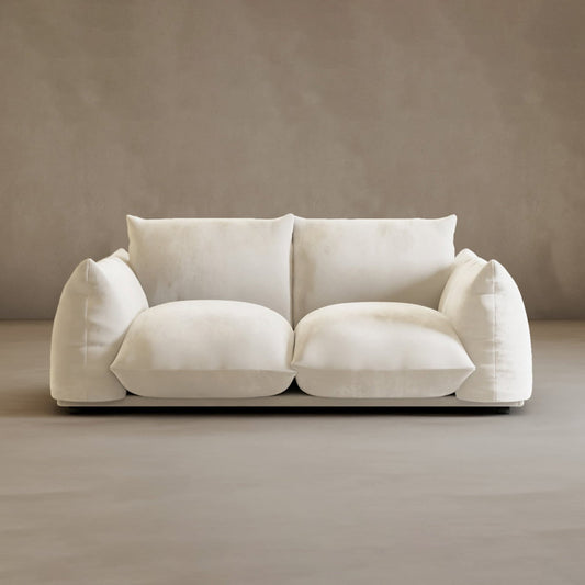 The Calypso Loveseat, featuring oversized cushions and a low-profile design, exudes modern elegance against a plain beige wall and floor.