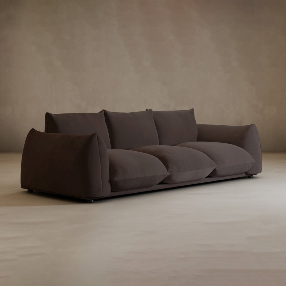 The Calypso Three Seater Sofa, in modern dark brown plush with wide cushioned arms and deep seats, stands in a minimalist room featuring beige walls and a light floor.