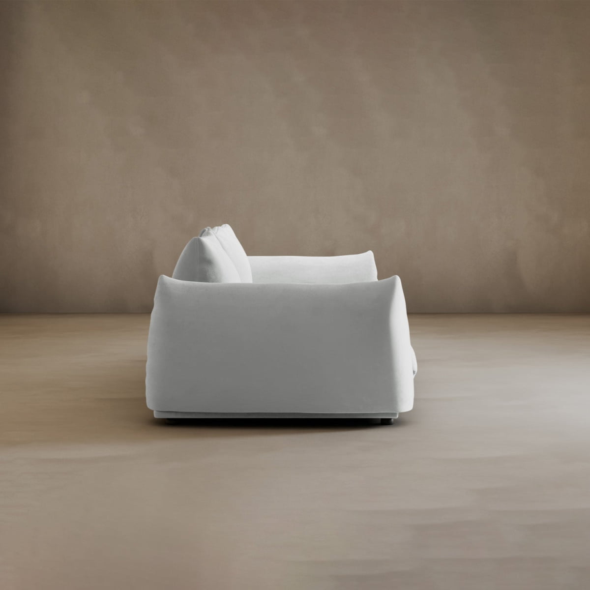 The Calypso Three Seater Sofa, featuring plush white cushions, is displayed side-on against a plain beige wall and floor for a minimalist yet serene look—perfect as stylish living room furniture.