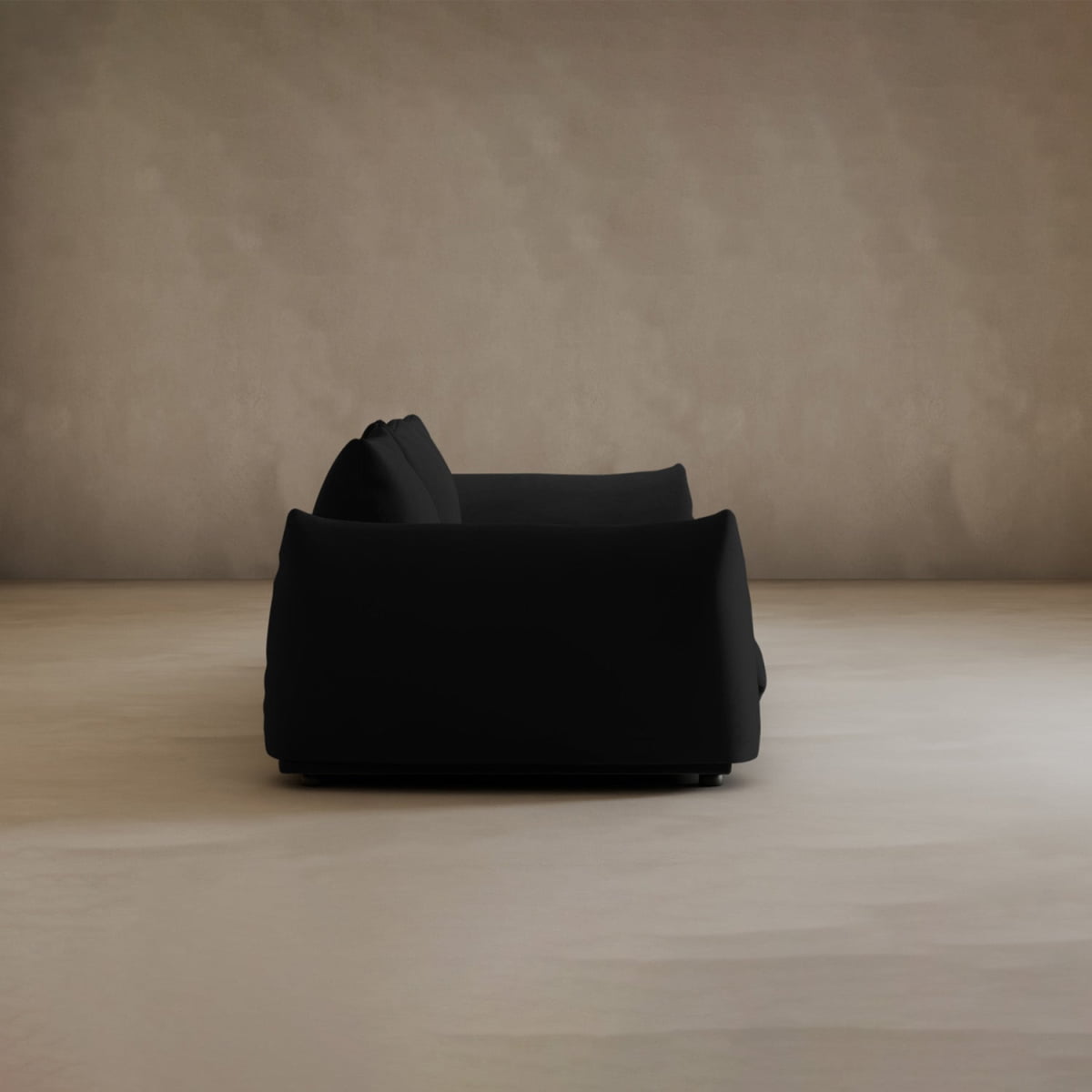 A black Calypso Three Seater Sofa with plush cushions sits in an empty room with beige walls and a smooth light floor, viewed from the side.