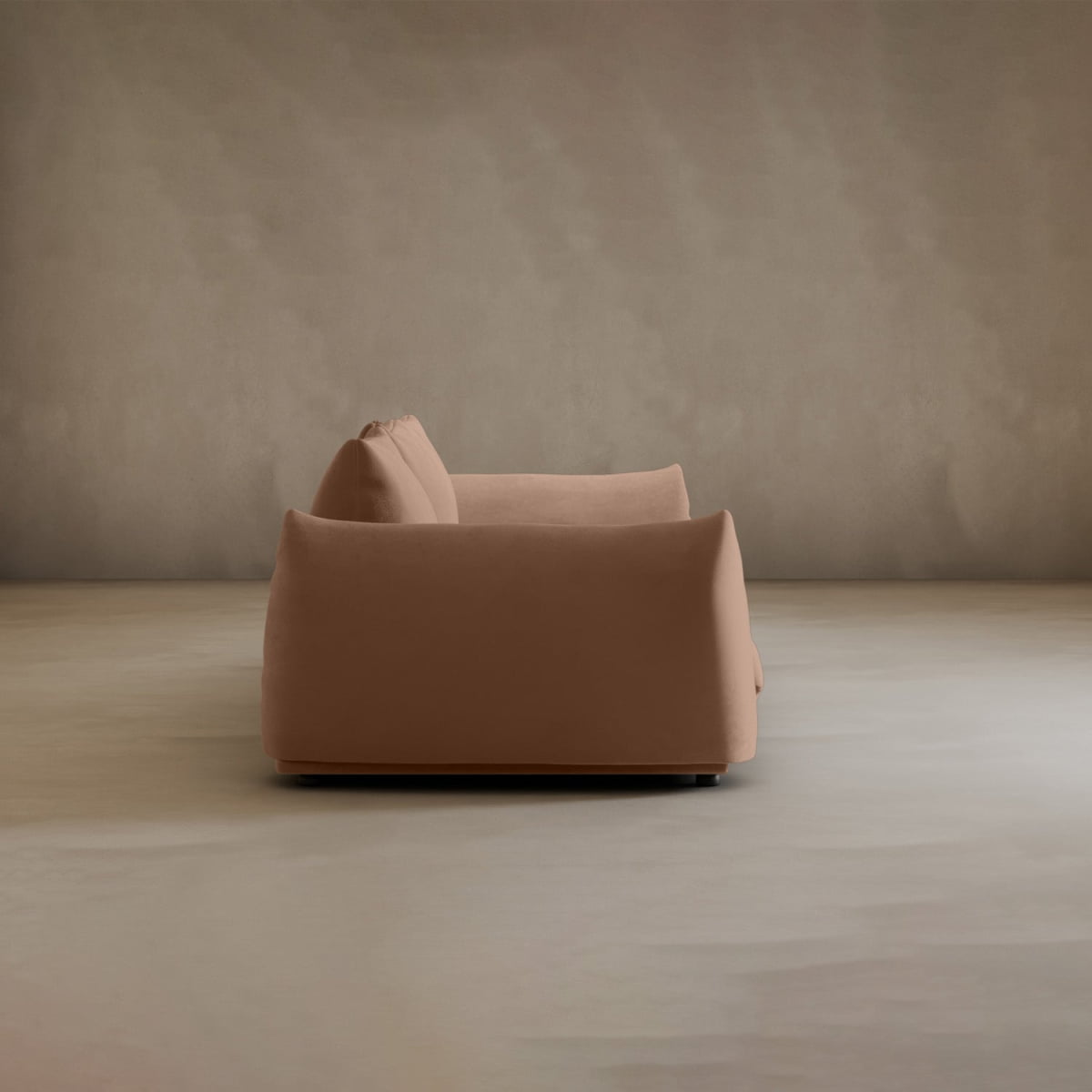 A modern, minimalist Calypso Three Seater Sofa with soft, rounded edges stands in an empty room featuring neutral walls and a matching floor, viewed from the side.