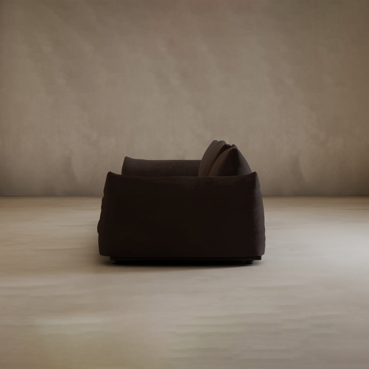 A Calypso Three Seater Sofa in dark brown is seen from the side in an empty room with beige walls and floor. The soft lighting highlights its modern design, creating a calm and minimalist atmosphere.