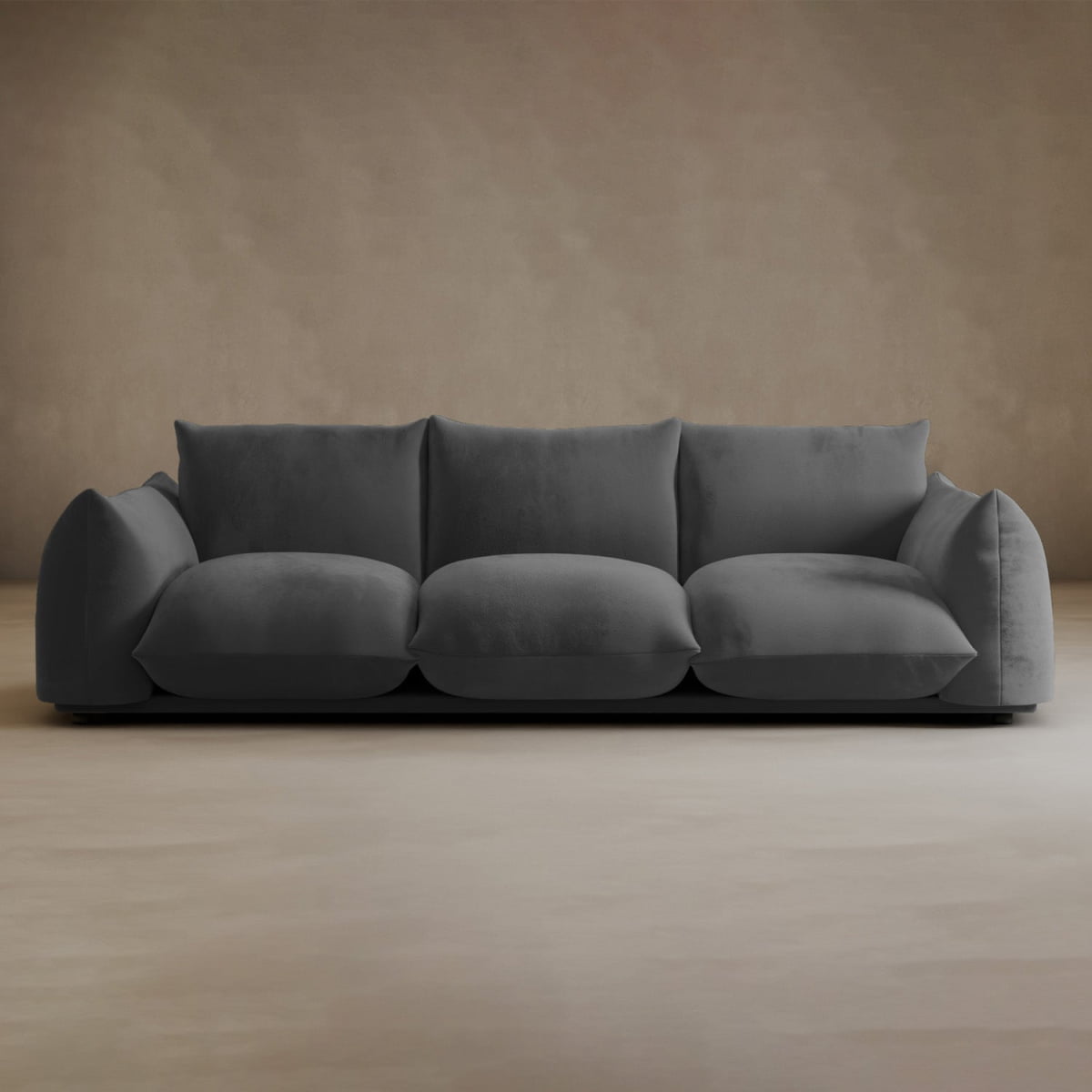 The Calypso Three Seater Sofa features plush cushions and wide armrests in dark gray, making it a modern choice for any living room with its low profile that complements beige walls and floors.