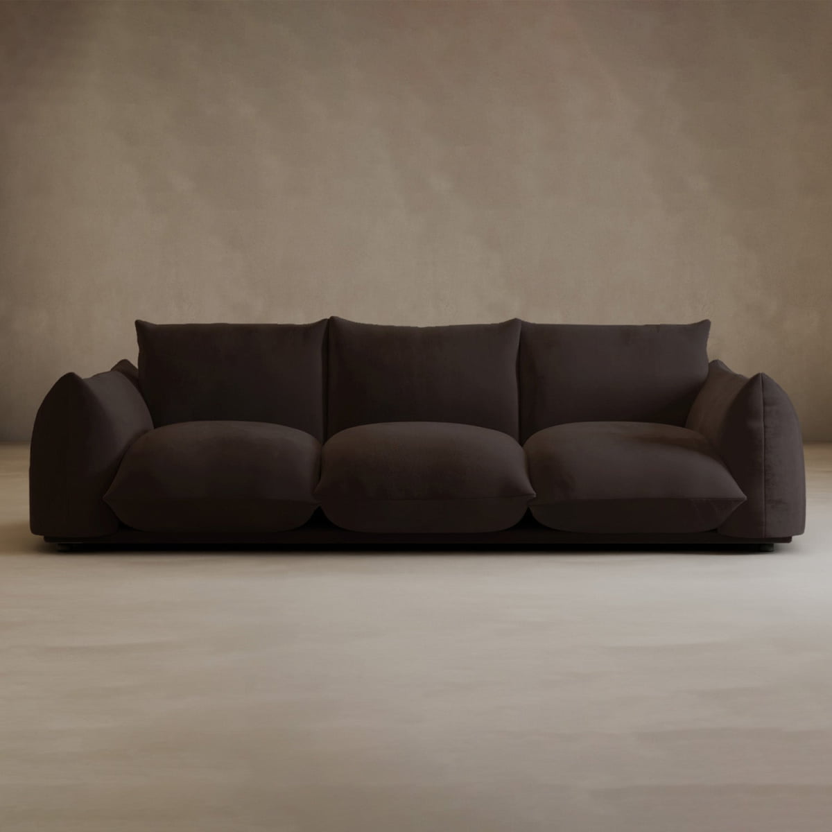 The Calypso Three Seater Sofa, featuring plush dark brown upholstery and oversized cushioned seats and backrests, stands out in an empty room with beige walls and flooring—ideal for modern living rooms.