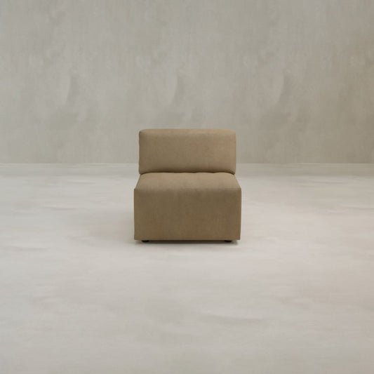 The Canonbury Middle Seat is a minimalist, armless chair upholstered in tan high-performance fabric, adding contemporary comfort to any space when placed on a light floor against a neutral, textured wall.