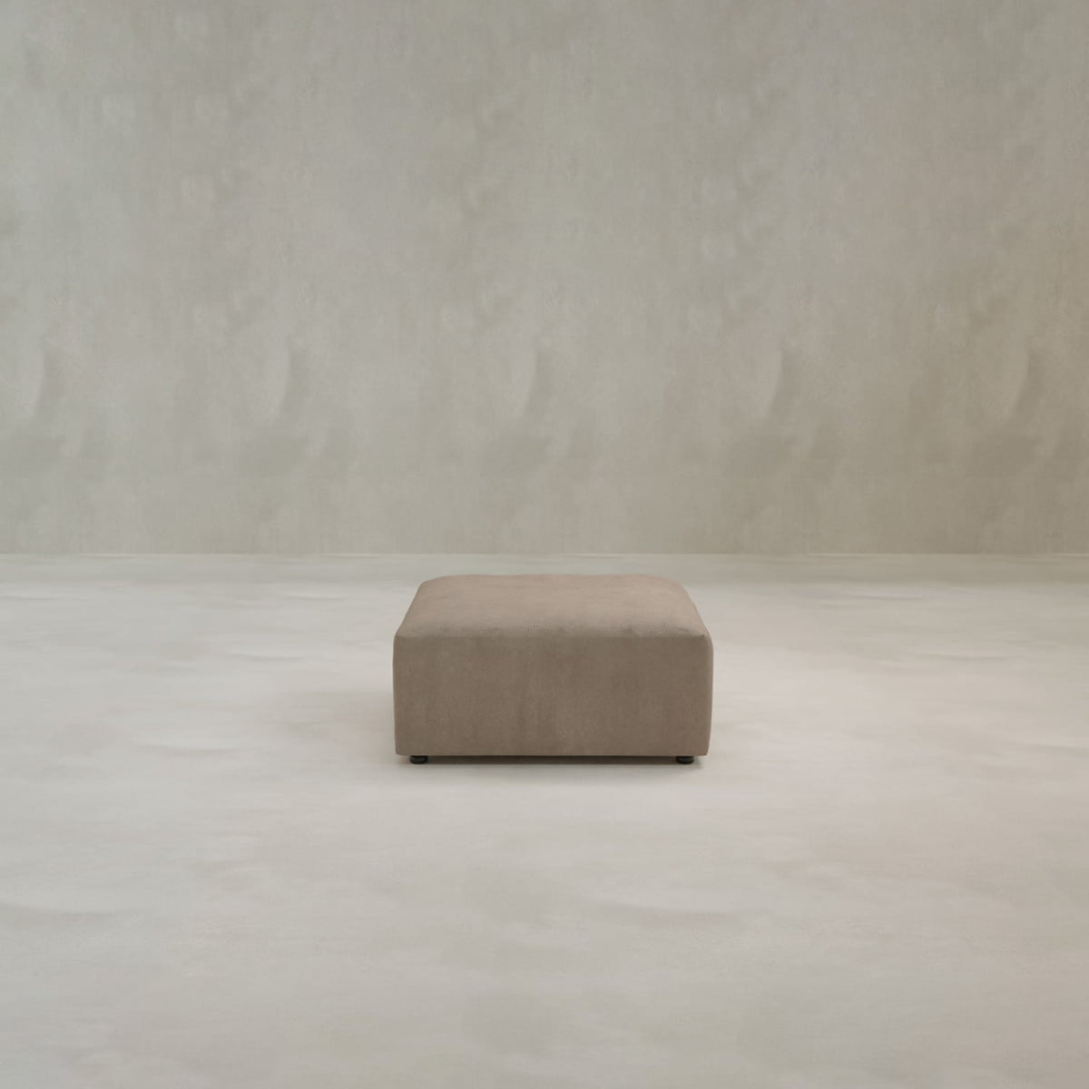 The Canonbury Ottoman, in a square taupe high-performance fabric, is centered in an empty room with light beige walls and a matching floor.