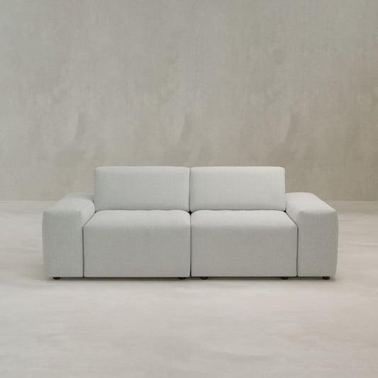 The Canonbury Two Seater is a modern, light gray sofa with wide square armrests and plush cushions, crafted from high-performance fabric—ideal contemporary comfort for any living space.