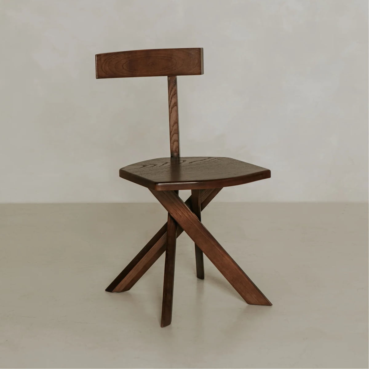 The Cartel Chair features bold angles, a geometric design, a flat seat, a simple horizontal backrest, and three angular legs, all set against a plain light background.