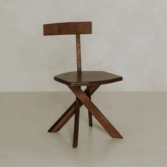 The Cartel Chair features bold angles, a geometric design, a flat seat, a simple horizontal backrest, and three angular legs, all set against a plain light background.