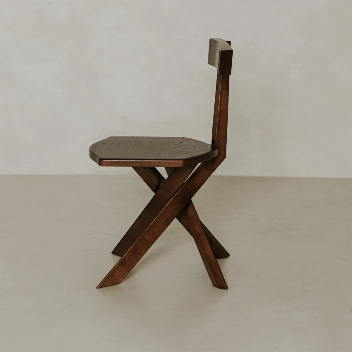 The Cartel Chair showcases bold angles and a geometric, angular design with a low rectangular backrest, set against a plain light-colored background.