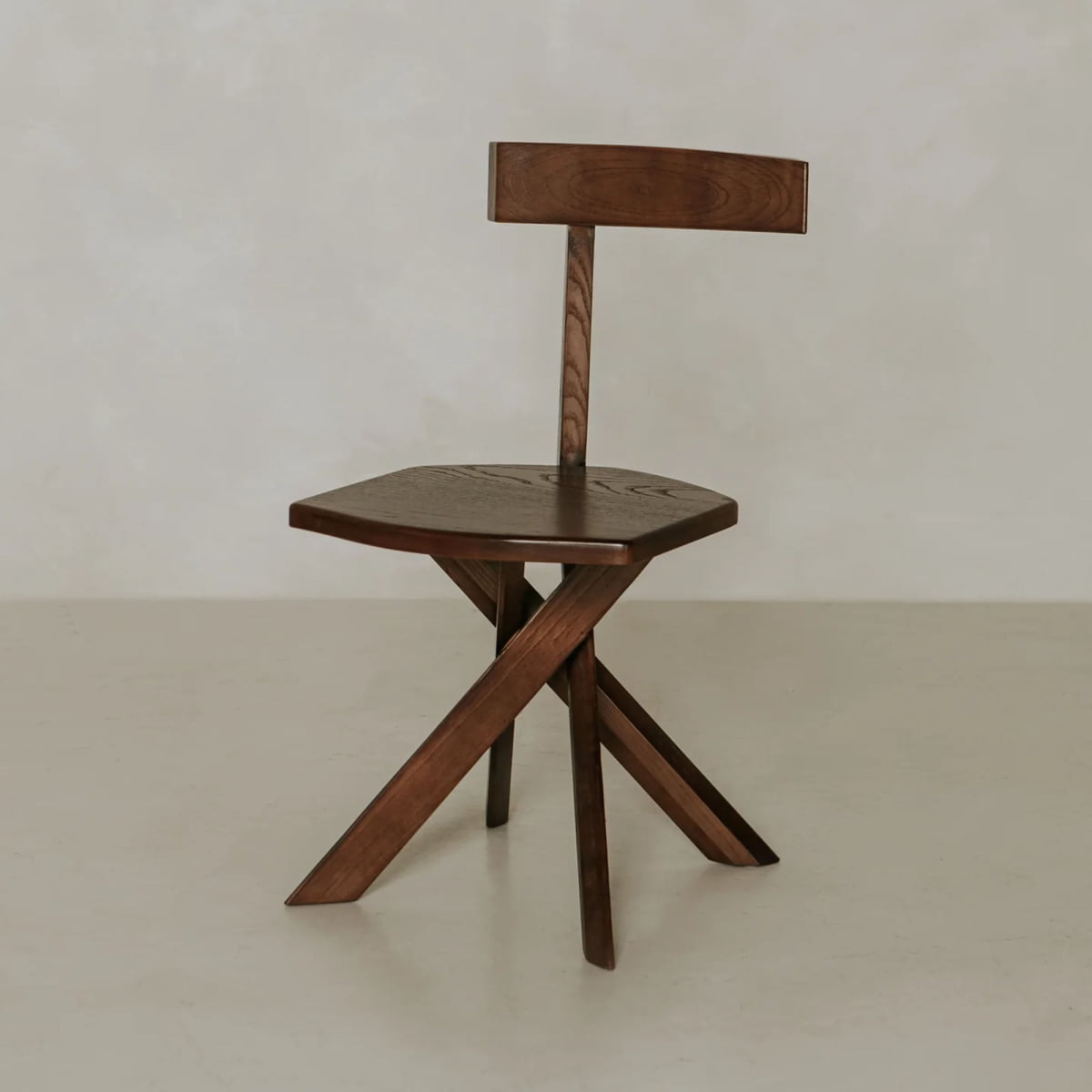 The Cartel Chair is a modern seat with bold angles, featuring an angular seat, crossed legs, and a straight rectangular backrest, displayed against a simple light background.
