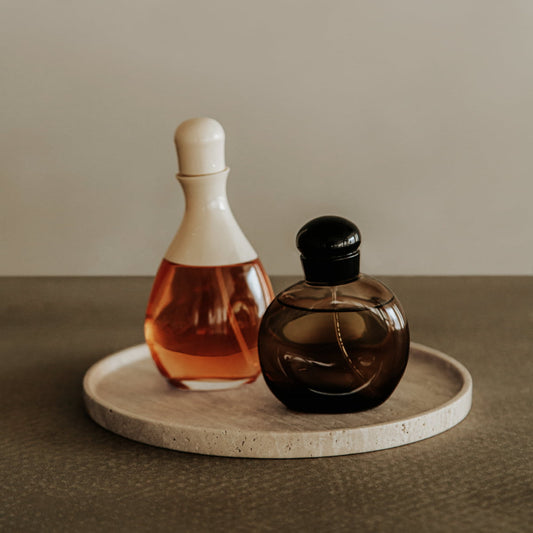 Two elegant perfume bottles—one clear with a white cap, the other dark with a black cap—are arranged on the Cascade Tray in Small, creating a naturally elegant decorative display against a neutral background.
