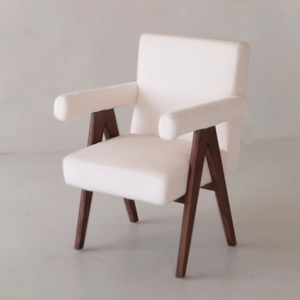 The Chelsea Dining Chair features comfortable vegan white upholstery, wooden angled legs, and armrests, presented against a plain light-colored background.