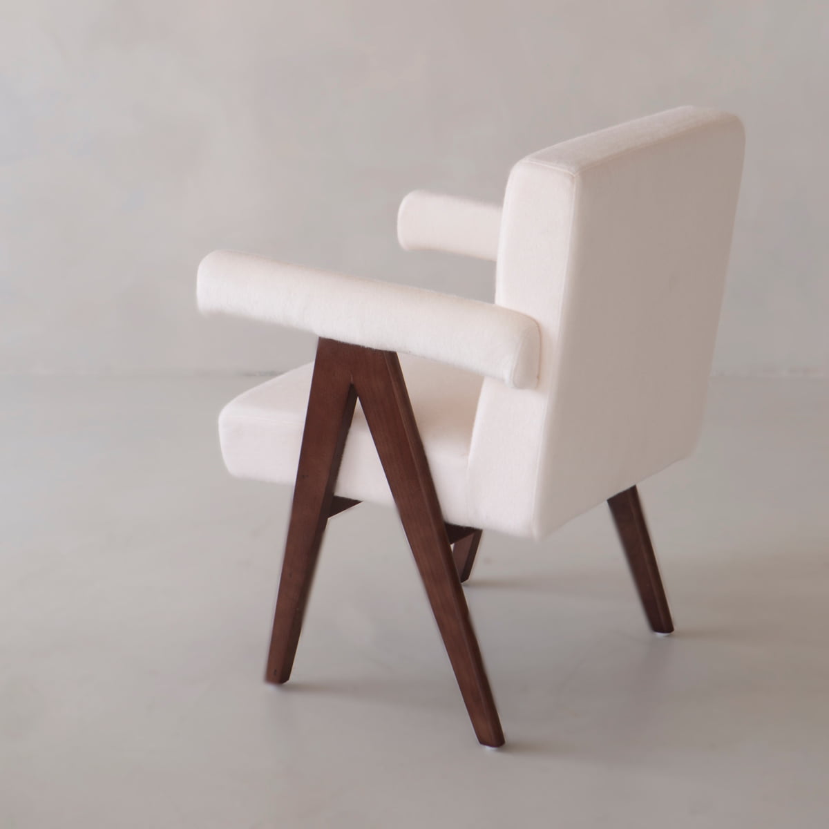 The Chelsea Dining Chair features vegan upholstered white fabric, dark wooden legs and frame, a minimalist angular design, and a padded seat for comfort. Shown on a light background.