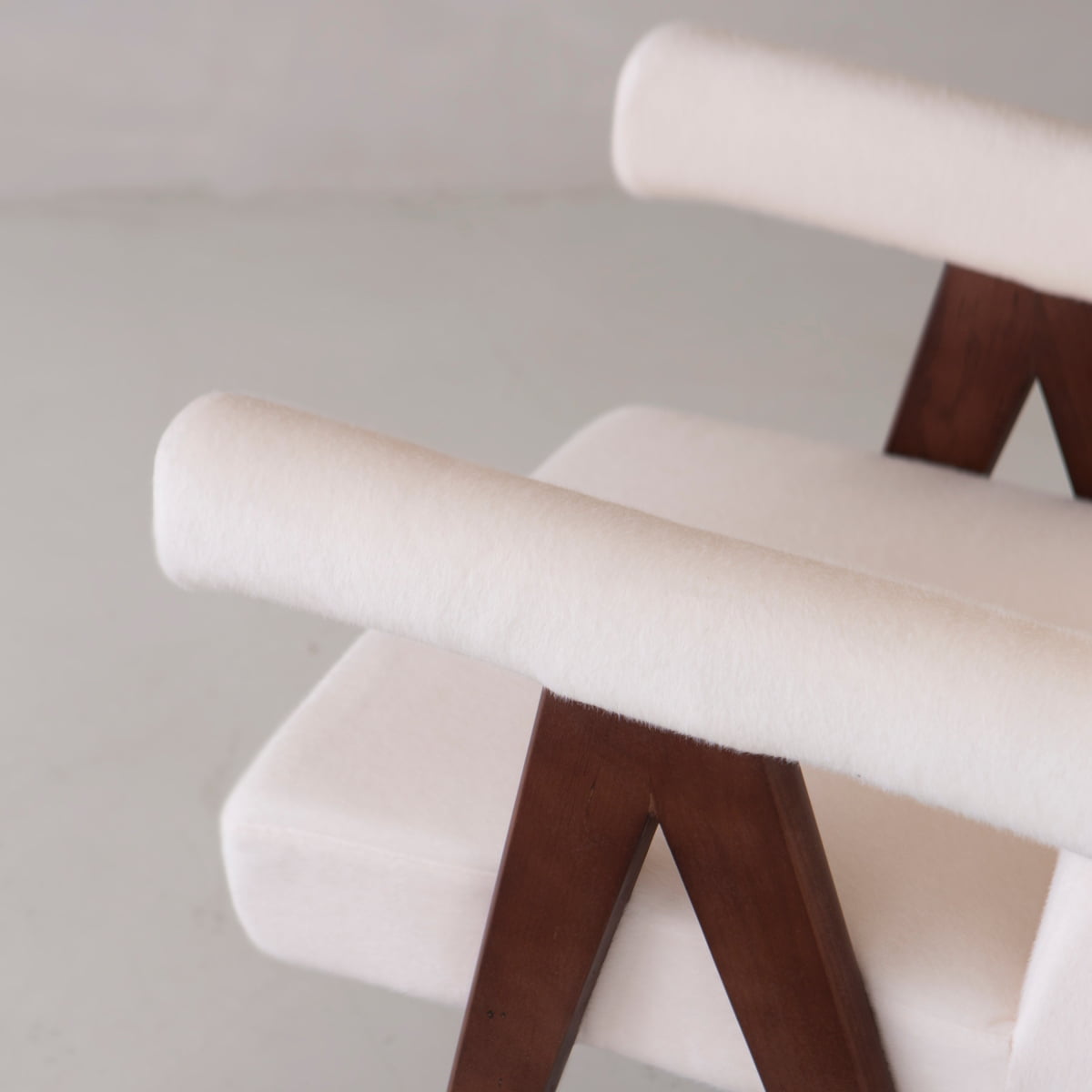A close-up of the Chelsea Dining Chair, featuring comfortable vegan-upholstered armrests, a padded seat, and dark wooden angled supports, set against a light background.