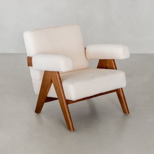 The Chelsea Lounge Chair boasts white faux mohair cushions with angled wooden legs and armrests, embodying mid-century style—ideal for placement on a light gray floor beside a plain light wall.