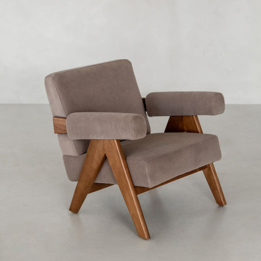 The Chelsea Lounge Chair, featuring faux mohair taupe upholstery and angled wooden legs and armrests, showcases a timeless mid-century style against a plain light gray background.