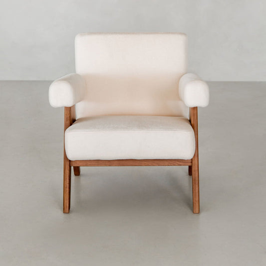 The Chelsea Lounge Chair features light beige faux mohair upholstery, wide cushioned arms, and a wooden frame, creating a refined mid-century look against a light gray minimalist background.