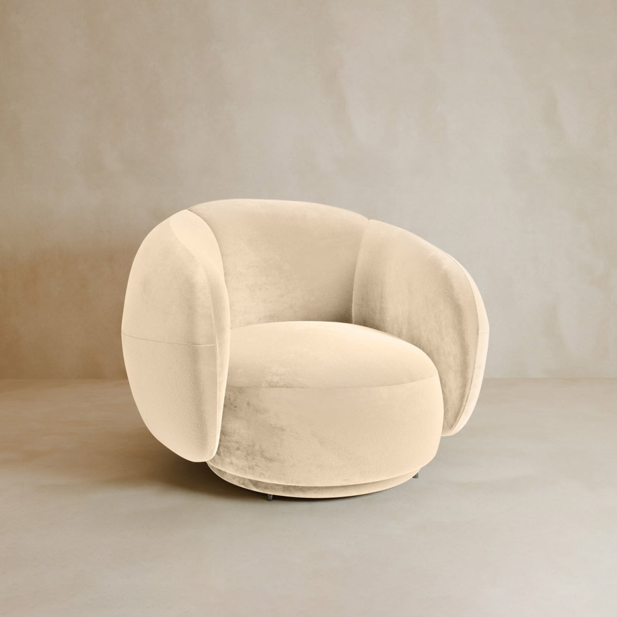 The Clara Armchair features plush beige velvet upholstery, rounded cushions, and wide arms, set against a light, minimalist backdrop.