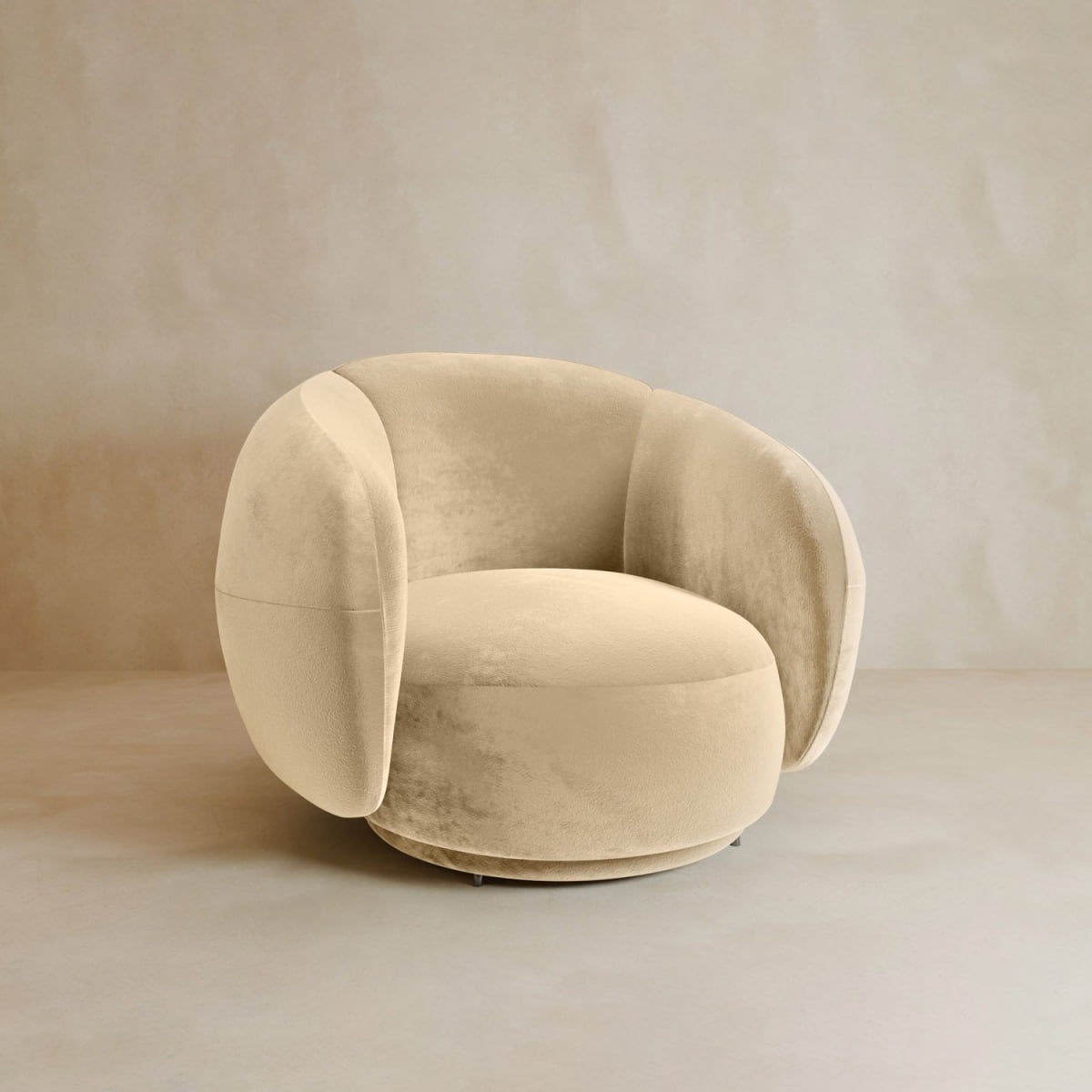 The Clara Armchair, a modern beige seat with plush, curved backrest and armrests, sits on a smooth neutral floor against a light beige wall.