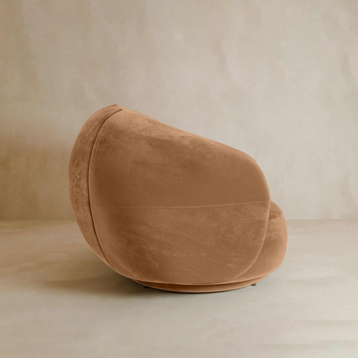 The Clara Armchair is a modern tan swivel chair with plush velvet upholstery, rounded minimalist design, and a cozy contemporary style, shown against a neutral textured background.